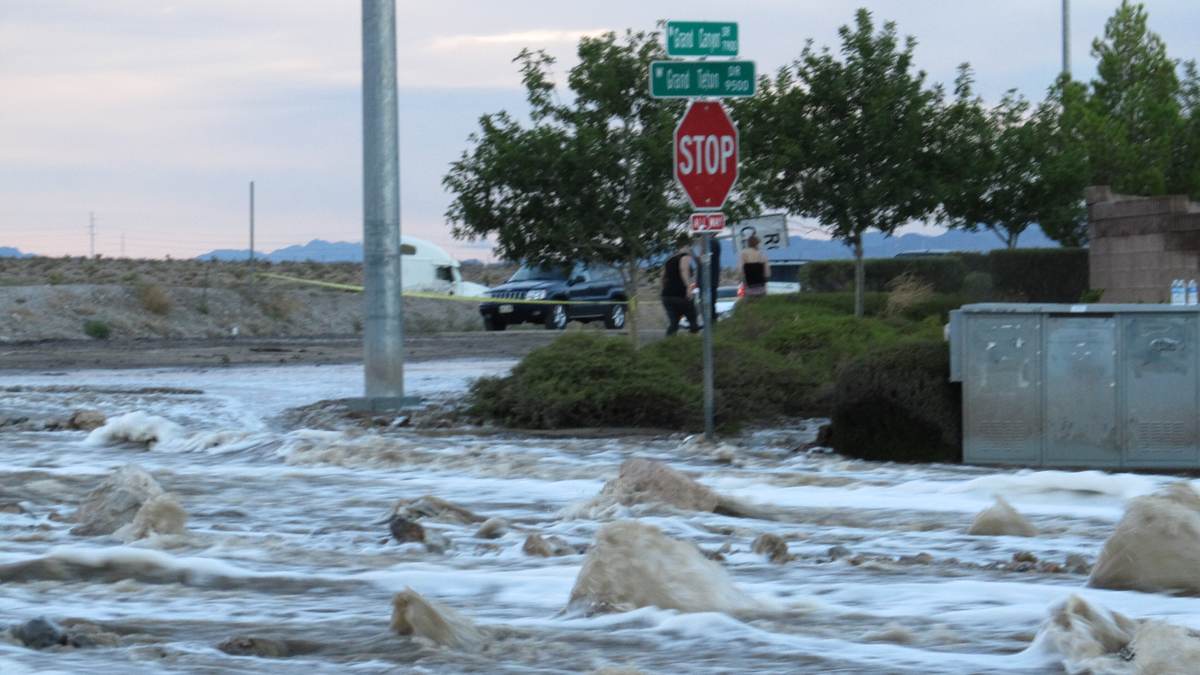 Brown floodwater running down Grand Teton Drive past a stop sign, a utility box and street trees